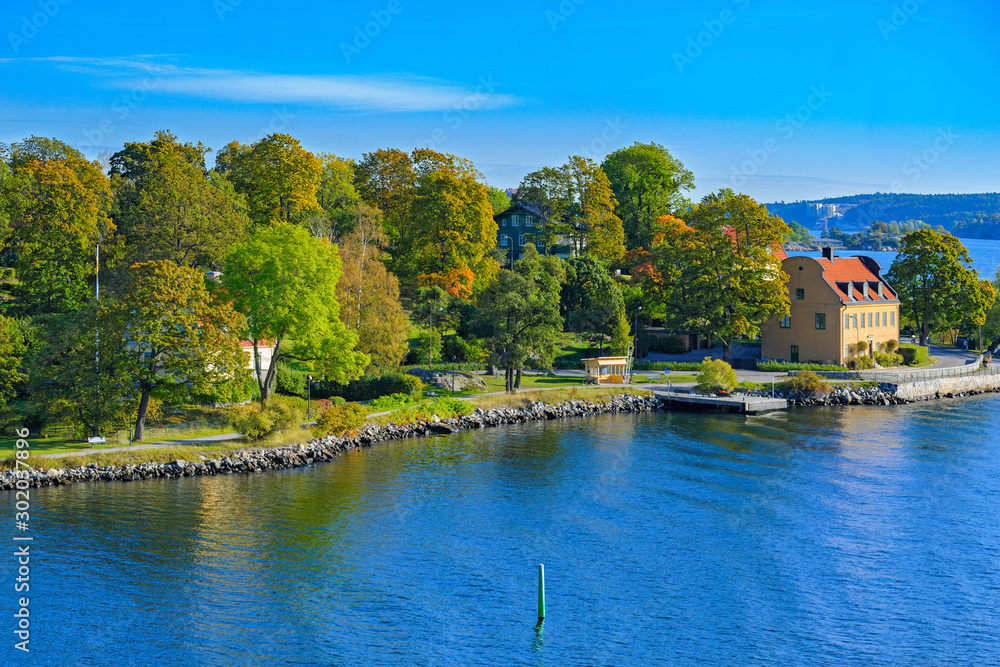 Seaside view of Djurgarden island with waterfront villas and colorful fall trees at autumn sunny morning. Stockholm, Sweden.