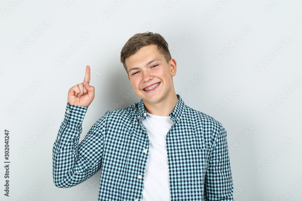 Young man with dental braces showing finger up on grey background Young man with dental braces showing finger up on grey background