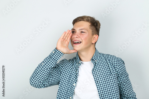 Young man with dental braces screaming on grey background