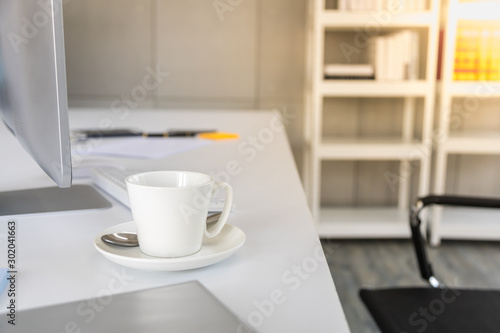 Business and workplace concept. Close up of white cup of hot coffee on work desk with computer and keyboard in office working room.
