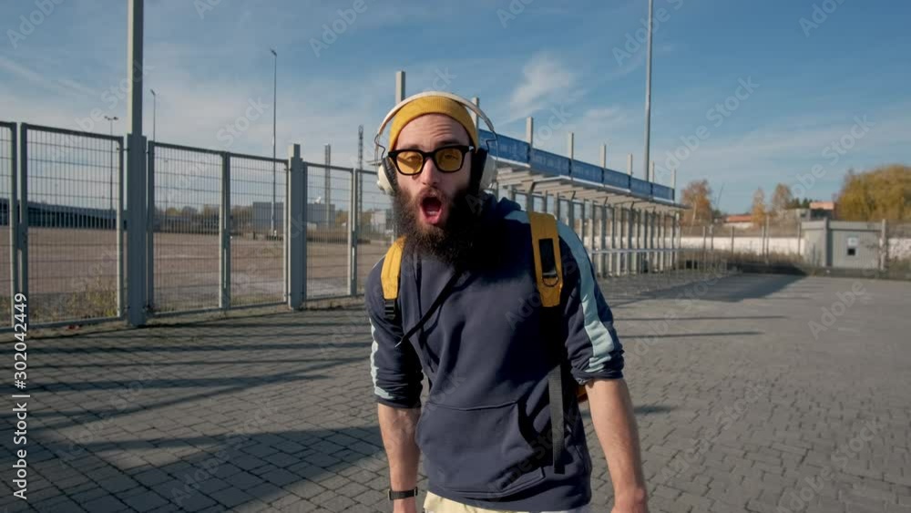 Portrait of a stylish bearded man in yellow clothes enjoying music with headphones on the blue sky background