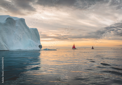 Beautiful red sailboat in the arctic next to a massive iceberg showing the scale Fototapet