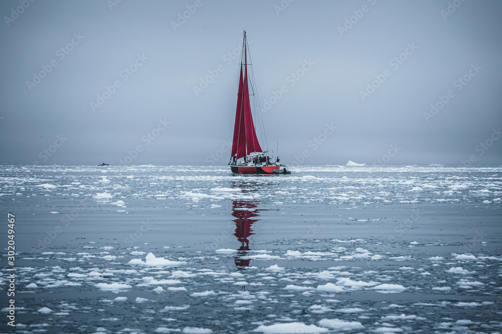 Naklejka premium A small boat among icebergs. Sailboat cruising among floating icebergs in Disko Bay glacier during midnight sun Ilulissat, Greenland. Studying of a phenomenon of global warming Ices and icebergs