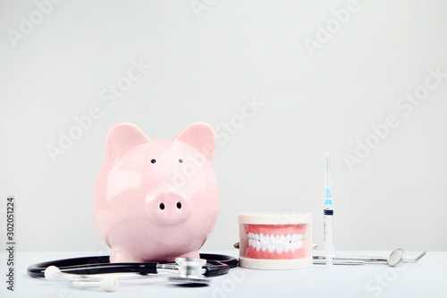 Pink piggy bank with stethoscope and teeth model on grey background