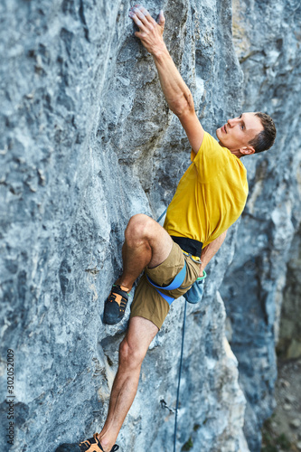 Young strong man climbing challenging route on a high vertical limestone cliff.