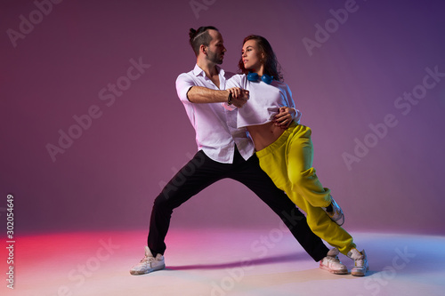 Professional couple of dancers passionately performing expressive dance, looking away, pay no attention to audience, modern style dancers in studio full of light