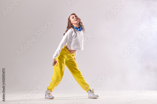 Professional young female dancer in motion, looking at camera with cheerful expression, stands on white floor with happily opened mouth, focused on training , isolated on white background