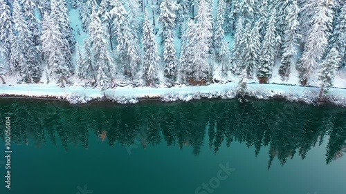 Forest in winter season and alpine lake, snow covered trees are reflected in the water