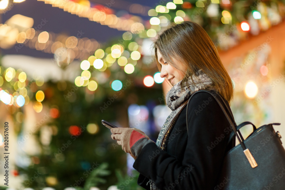 Photo side of girl with phone in hand on street in evening on blurred background with garland Photo side of girl with phone in hand on street in evening on blurred background with garland