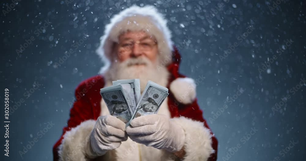 Santa clause looking at camera and showing packs of money in his hands, isolated on blue snowy background - christmas spirit concept close up 4k footage Santa clause looking at camera and showing packs of money in his hands, isolated on blue snowy background - christmas spirit concept close up 4k footage