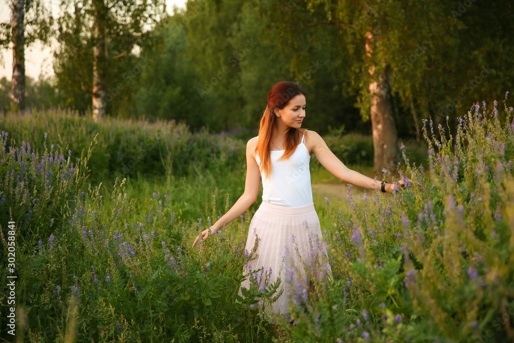 carefree girl walking in the wild flowers field. female stroking flowers in a field