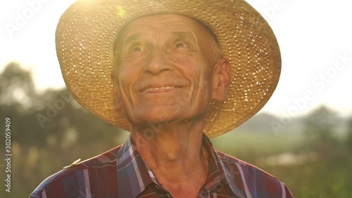 happy senior man in straw hat smiles looking around beautiful countryside under warm summer sun slow motion close view photo