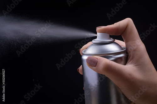 Female hand holds an aerosol can on a black background. photo
