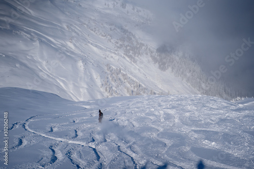 Image of a snowy surface covered by ski marks and man skiing down © nuclear_lily