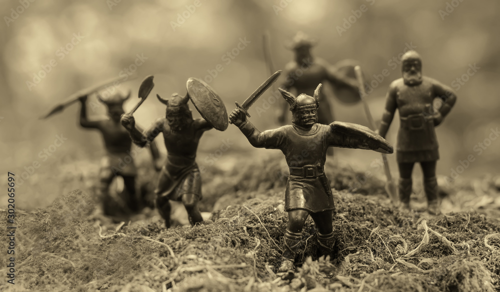 Five well armed attacking Vikings (toy soldiers), located on a mossy place, misty blurred background, selective focus, Old Norse Gods, Valhalla topic, epic myths, monochrome photo (sepia) - obrazy, fototapety, plakaty 