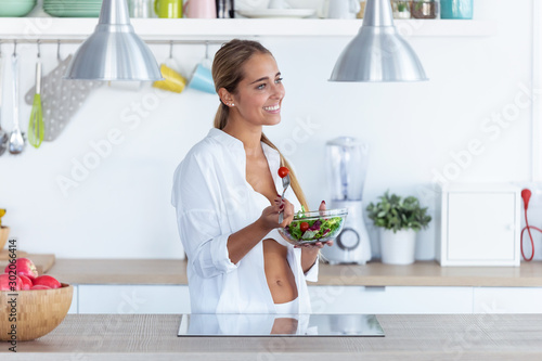 Pretty young woman in underwear eating salad in the kitchen at home.