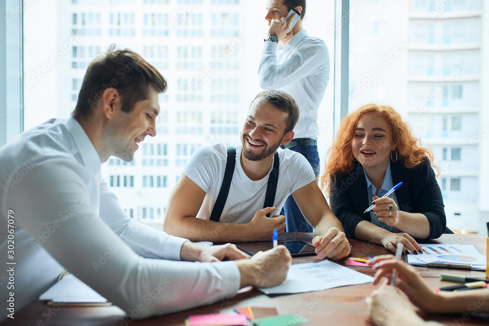 Caucasian creative colleaguew work together, discuss new issues of work, business team. Modern office with panoramic view on city background Caucasian creative colleaguew work together, discuss new issues of work, business team. Modern office with panoramic view on city background