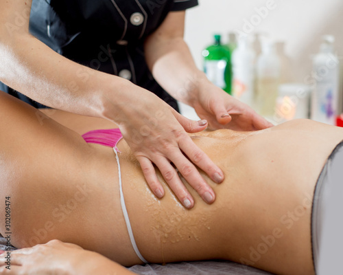masseuse applies honey on the body of a woman on a massage table. Honey massage in the spa
