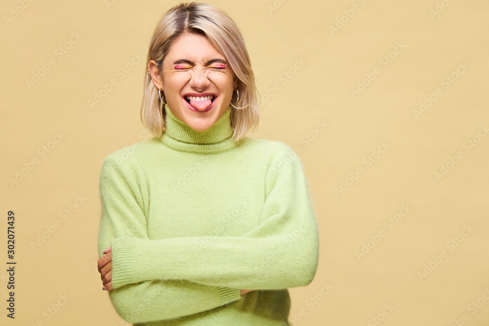 Studio shot of emotional young European cute blonde woman sticking out