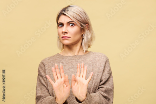 Portrait of outraged furious young European blonde woman expressing indignation, reaching out hands, making No or Stop gesture, saying Stay away from me while having fight with her boyfriend photo