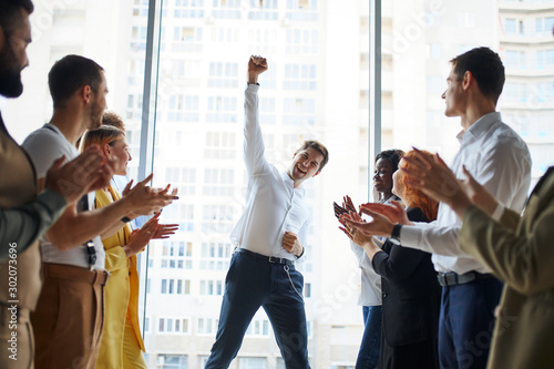 Happy business team is clapping their hands in modern workstation, celebrating the performance of new product of their man colleague working together photo