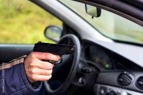 Man with a gun driving a car, male hand with a gun