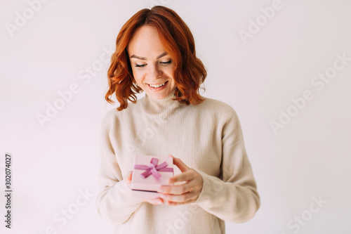 Young birthday girl smiles  holding a pastel coloured gift box with pink ribbon. Happy woman  peeking inside a gift box.