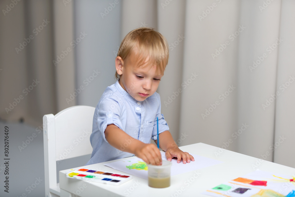 Cute little boy paints with watercolors while sitting at the tab Cute little boy paints with watercolors while sitting at the tab