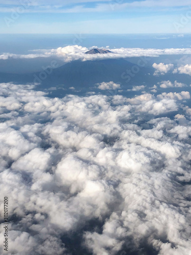 Aerial view of Agung volcano peak in Bali from plane window. Cloudy beautiful weather.