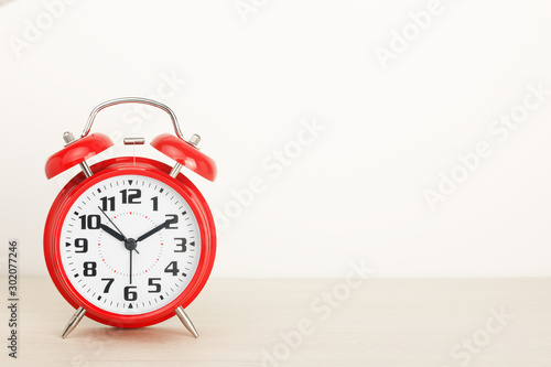 Red retro alarm clock, with a large dial on a wooden table on a white background. The concept of time, delay, morning rise, the appointed meeting. Layout with copy space for your text.