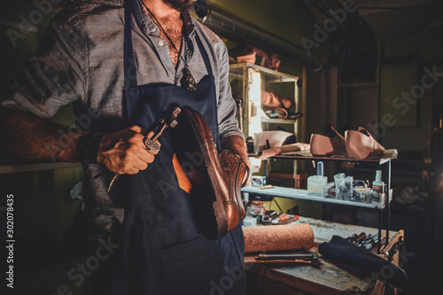 Fototapeta Naklejka Na Ścianę i Meble -  Diligent cobbler is working on shoe sole using special tool at his dark workplace.