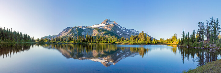 Volcanic mountain in morning light reflected in calm waters of lake. 