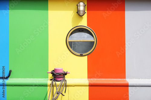 Foto Colorful metal boat wall with round glass window, lamp, rope and pink bollard