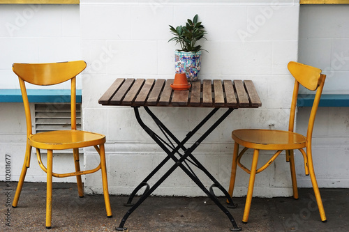 Yellow chairs and outdoor wooden table by the rough white wall decorate with small plant on the table