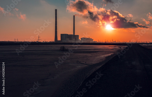smoking chimney of a factory against fiery orange sunset. colorful and speckled clouds.