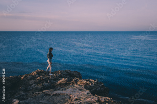 Woman traveler standing near sea on top of cliff in summer mountains and enjoying view of sea and nature. Cape Greco, Cyprus, Mediterranean Sea. Sunrise