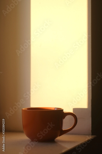 Cup of tea on a window sill, illuminated by warm sunset light. Selective focus.