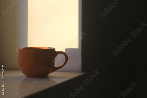 Cup of tea on a window sill, illuminated by warm sunset light. Selective focus.