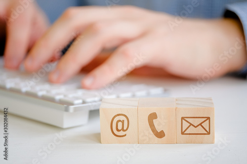A man is typing on a keyboard next to wooden cubes with a symbol of email, telephone and letter. Contact concept for communication.