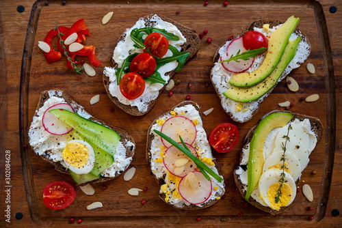 Five sandwiches with fresh vegetables, tomatoes, cucumbers, radish and eggs on a blue wooden background. Homemade butter and toast.