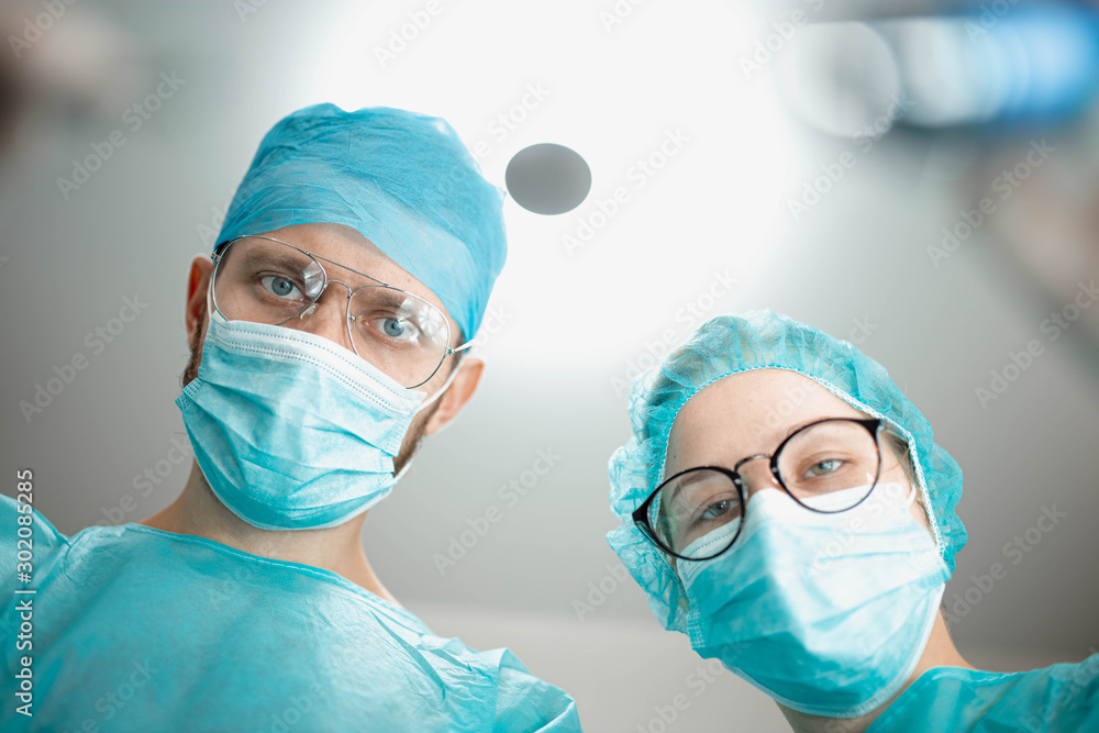 Professional surgeon with a young female assistant intern in a hospital operating room. Shot from a lower angle, surgery. Professional surgeon with a young female assistant intern in a hospital operating room. Shot from a lower angle, surgery.