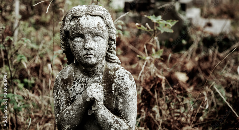 Ancient statue of a praying angel with broken wings as symbol of pain.