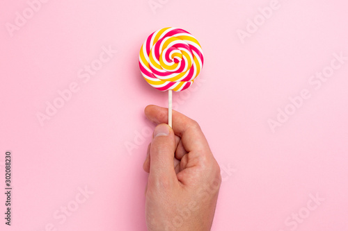 Colorful lolipop in hand , pink, yellow and white spiral on pink background , childhood sweets