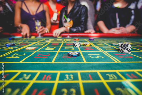 A close-up vibrant image of multicolored casino table with roulette in motion, with casino chips. the hand of croupier, mone and a group of gambling rich wealthy people in the background