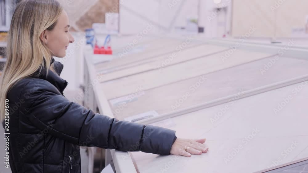 Beautiful young girl chooses a ceramic tile at the hardware store. The concept of shopping, construction, interior design Beautiful young girl chooses a ceramic tile at the hardware store. The concept of shopping, construction, interior design