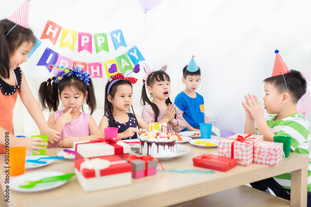 Fototapeta premium pretty asian children blow out candles on birthday Cake, asian children group meeting in celebration party, they sing happy birthday song and clasp hand, happiness activity
