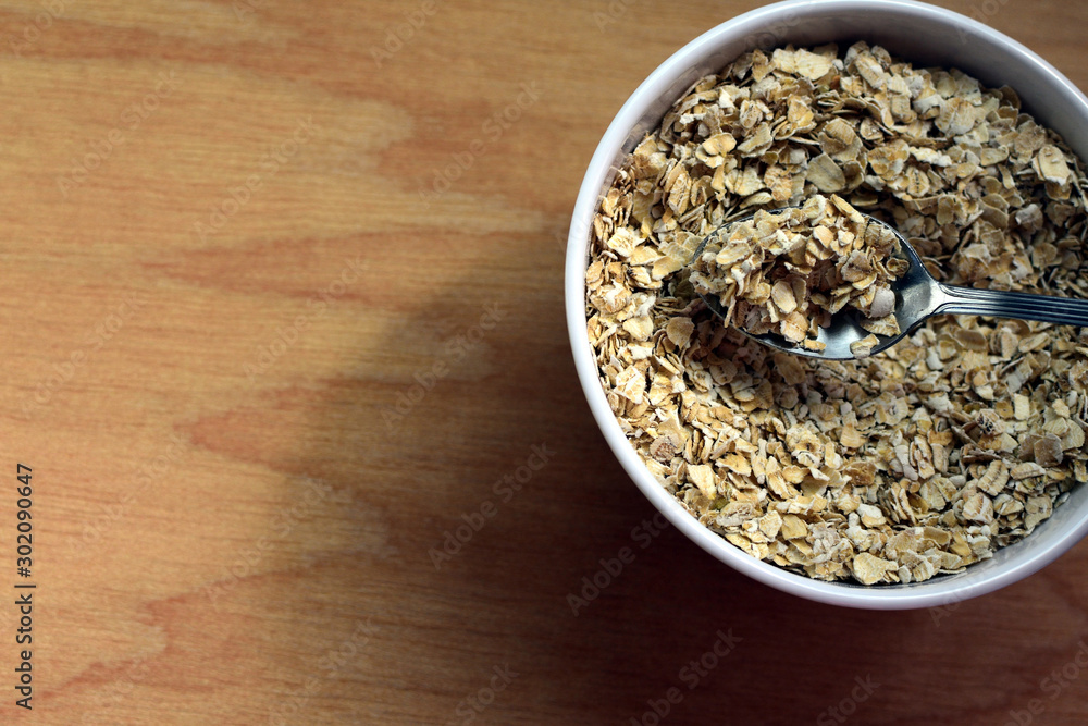 Bowl of raw oatmeal with spoon on wooden background Bowl of raw oatmeal with spoon on wooden background