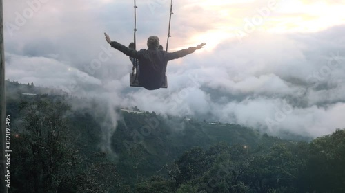 Man on a wooden swing with open arms flying above Ecuadorian Mountains in a foggy day. Slow motion