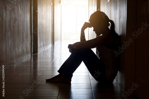 Silhouette of depressed woman head bending touch her hand sitting lean against the wall