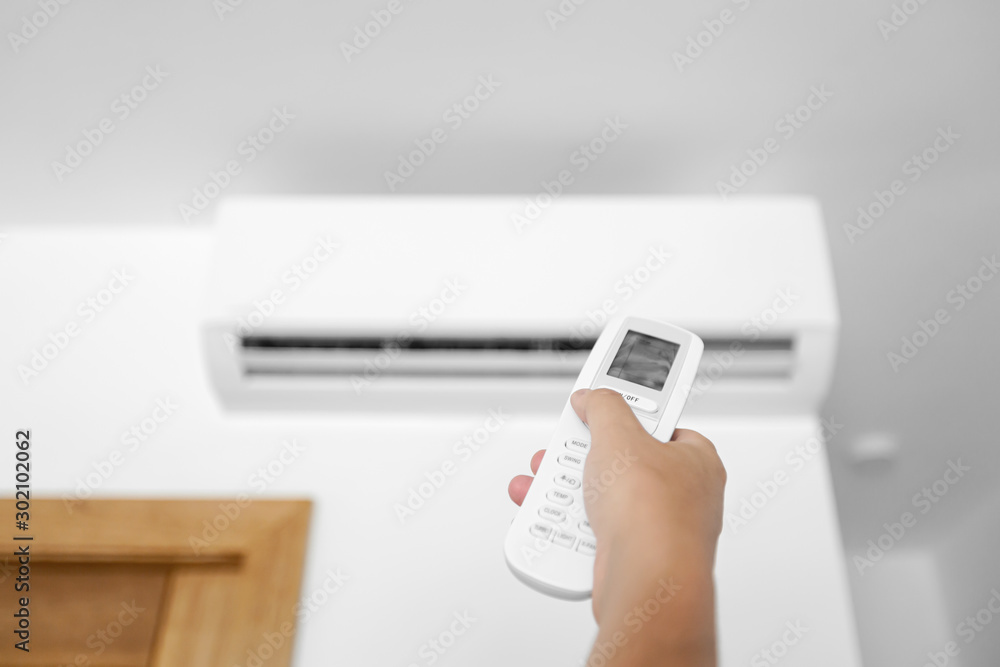 Flat air conditioner on white wall in room interior. Man pushing button on remote Flat air conditioner on white wall in room interior. Man pushing button on remote